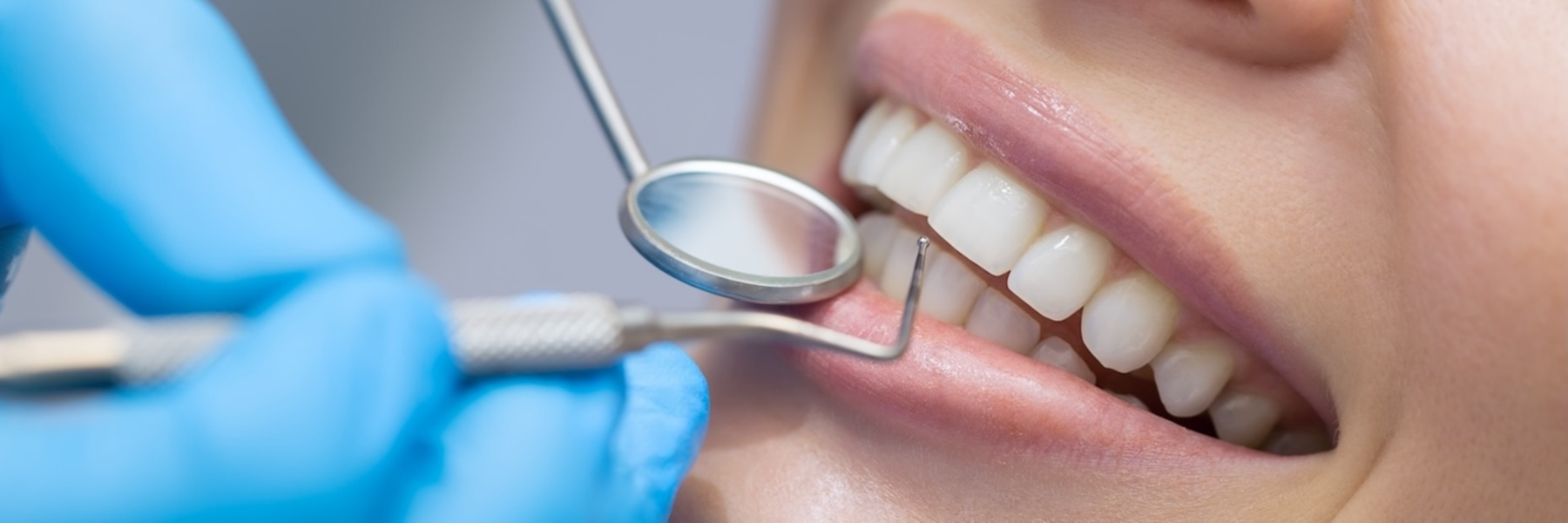 Dentist using mirror tool to examine patient's healthy white teeth during dental hygiene checkup